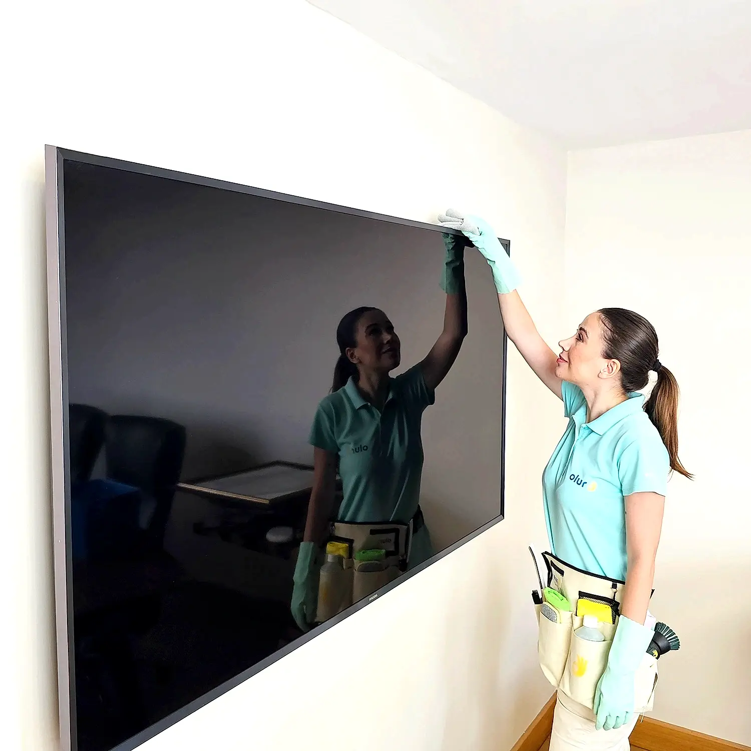 Günlük temizlikçi kadın, ev temizliğinde mikrofiber bez ile televizyonun tozunu alıyor